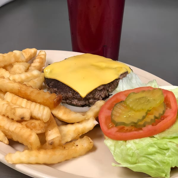 A cheeseburger with lettuce, tomato, and pickles, served with crinkle-cut fries and a red drink.