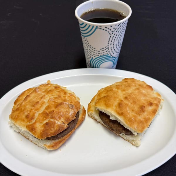 Two sausage biscuits on a white plate with a cup of coffee at Kelly's Restaurant.