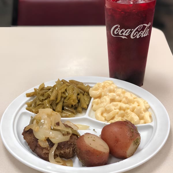 A southern meal with hamburger steak, onions, green beans, macaroni and cheese, and red potatoes.